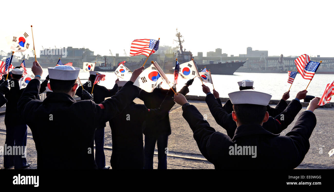 Republic of Korea sailors wave flags as they welcome the Arleigh Burke-class guided-missile destroyer USS Mustin during a port visit January 11, 2015 in Donghae, South Korea. Mustin is stationed in Yokosuka, Japan, as part of the forward deployed U.S. 7th Fleet. Stock Photo