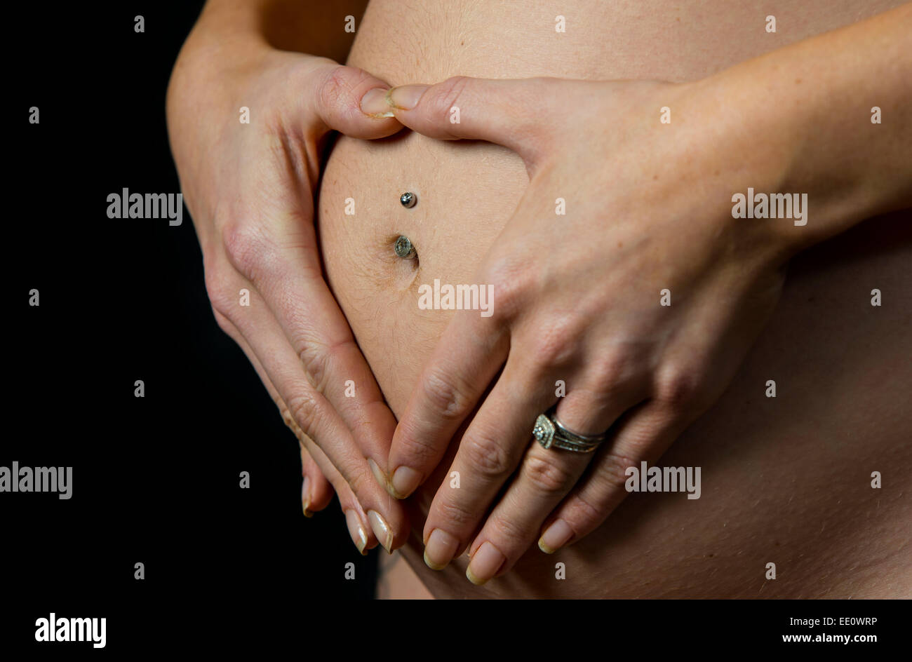A woman holds her hands on her stomach or bump whilst pregnant creating a heart shape symbolizing love. Stock Photo