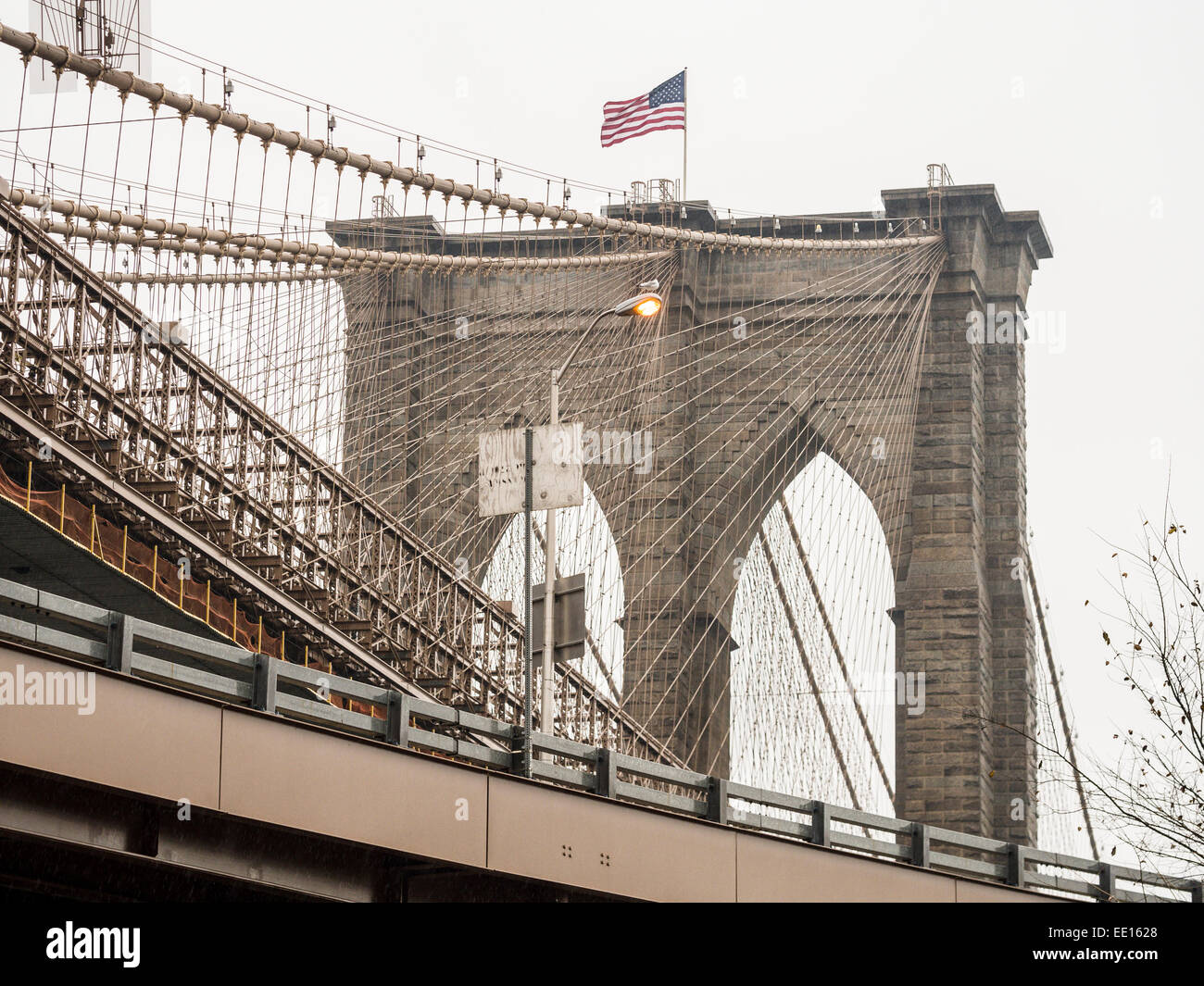North Tower of the Brooklyn Bridge. Suspension wires and an American flag dominate this image of the famous bridge from below. Stock Photo