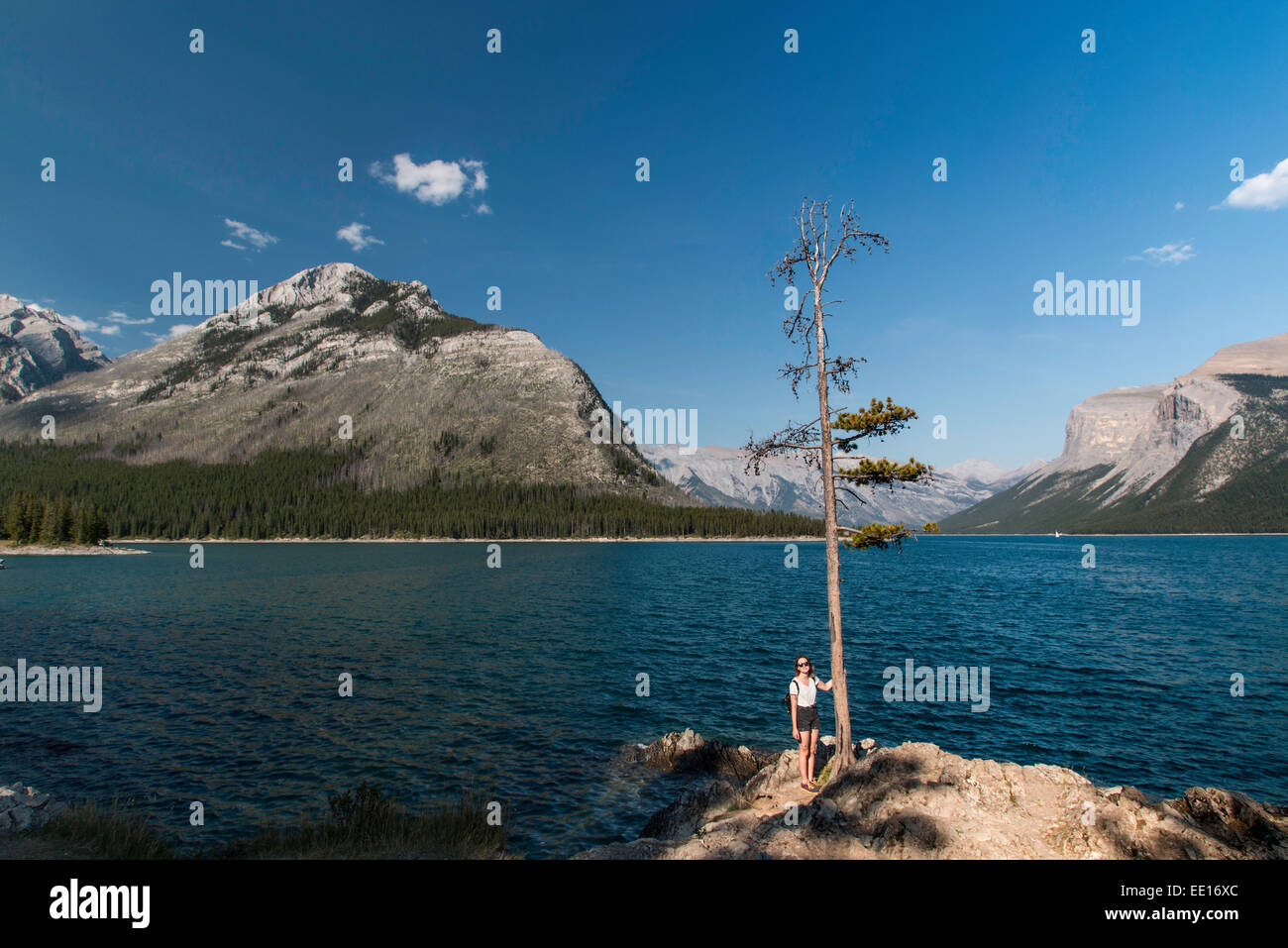 A young woman standing on a large rock at Lake Minnewanka in Banff National Park in Canada during summer Stock Photo