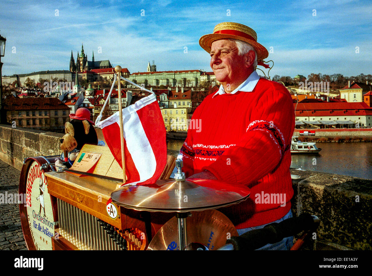 Senior man Musician play on barrel organ, Charles Bridge Prague Castle Czech Republic Europe busker street performer Prague musician Austrian Flag Stock Photo