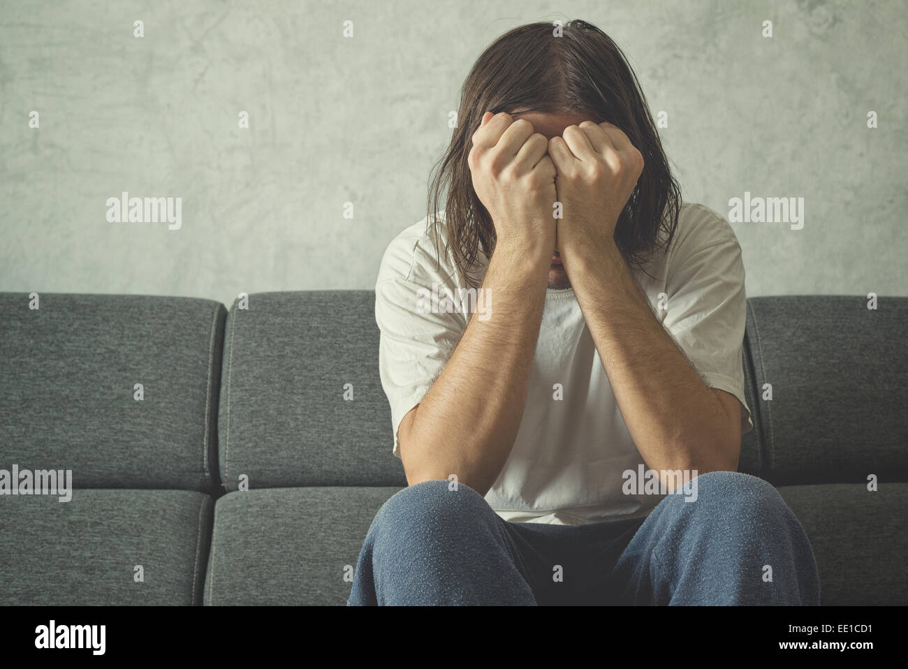 Depressed and sad man on the couch in the room, covering face and crying in despair. Stock Photo