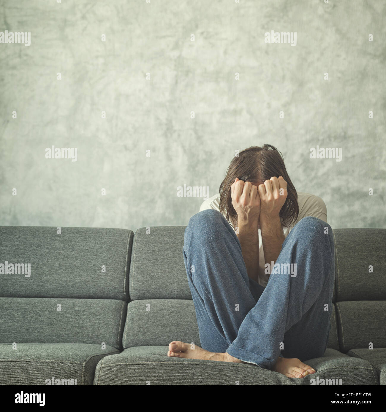 Depressed and sad man on the couch in the room, covering face and crying in despair. Stock Photo