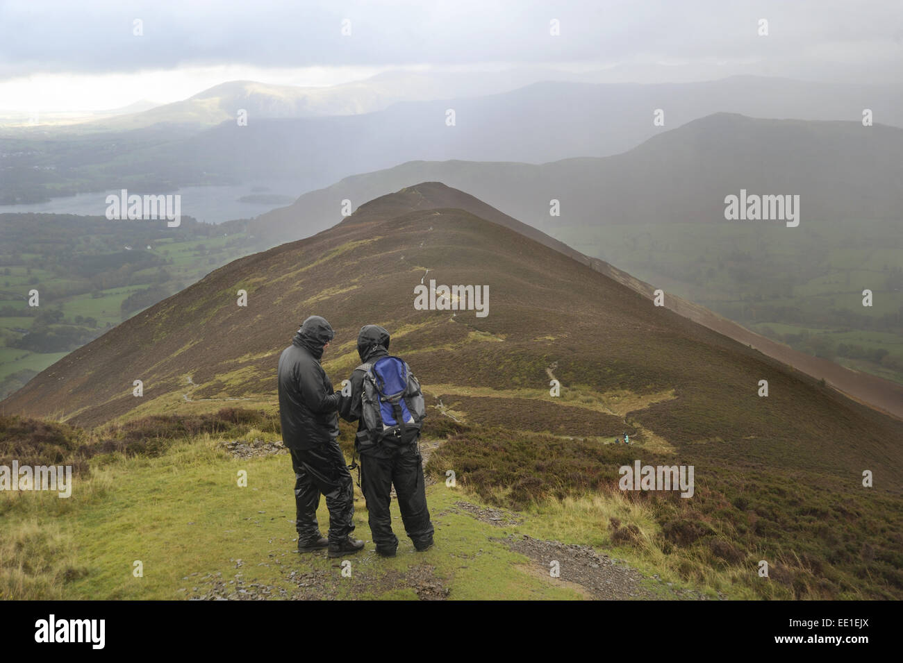 Walkers wearing waterproof clothing, looking at map during rain shower, view from Causey Pike, with distant views of Catbells and Derwentwater, Lake District N.P., Cumbria, England, October Stock Photo
