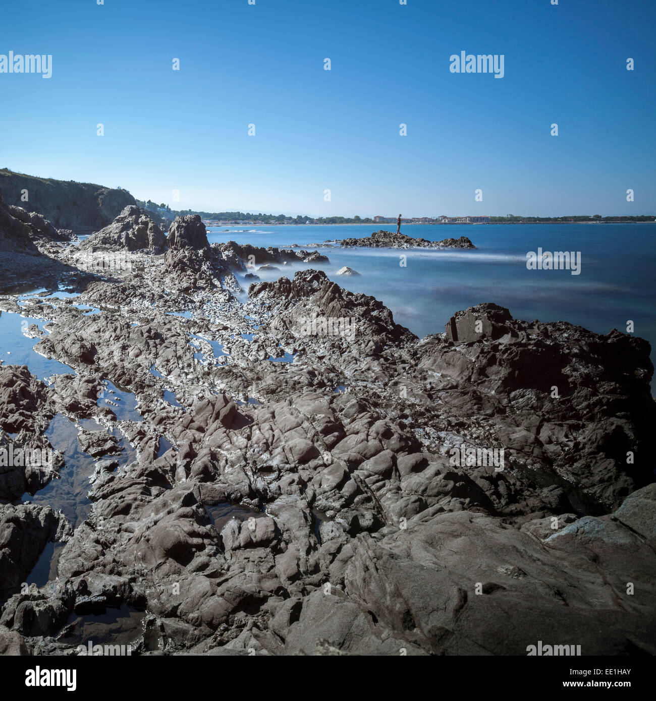 Rocky beach at low tide with man fishing on rock, Argelles, France, Europe Stock Photo