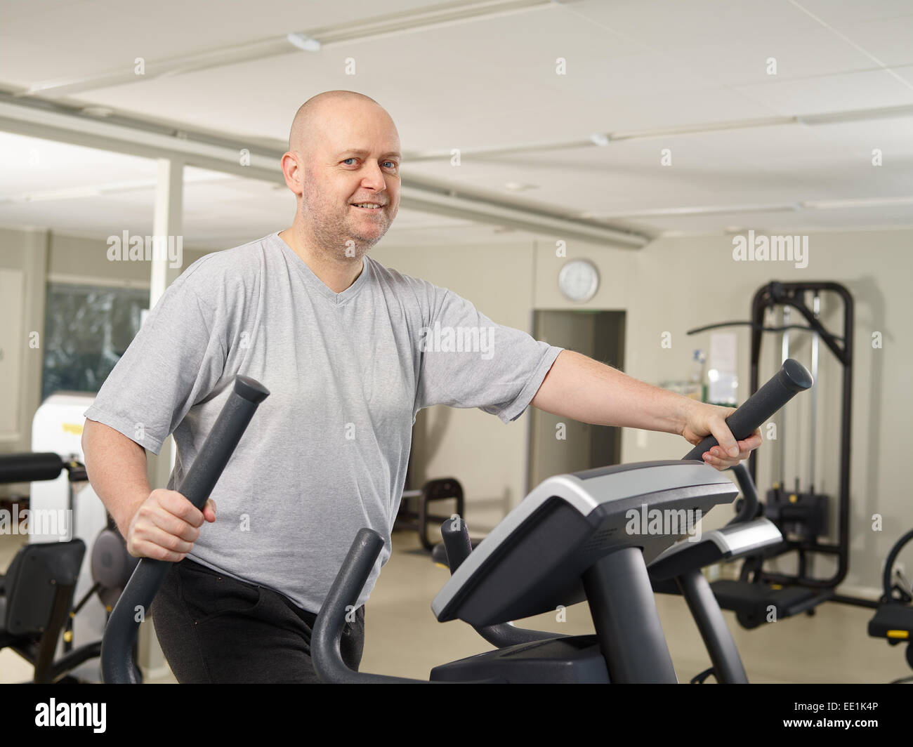 Mature man takes care of his health and he use elliptical trainer in the gym Stock Photo