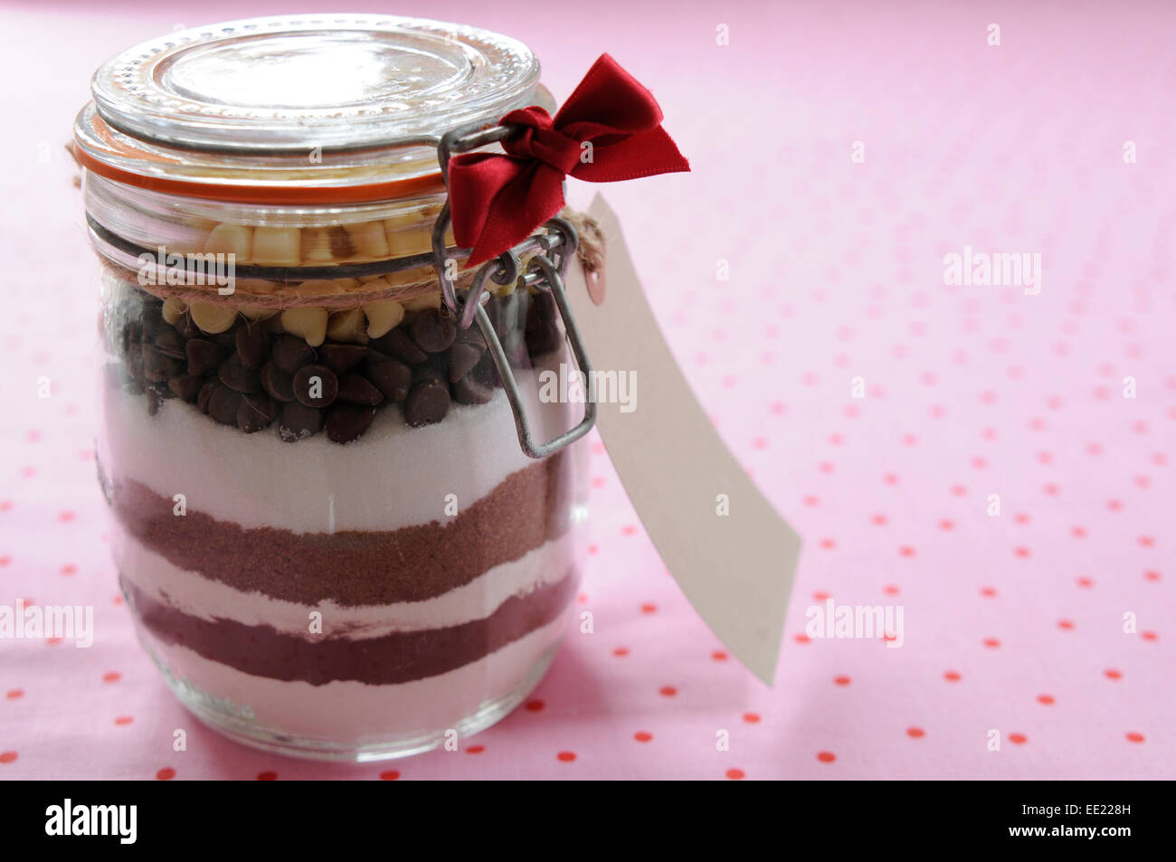 glass jar filled with ingredients to make chocolate chip cookies, on a pink and red polka dot background Stock Photo