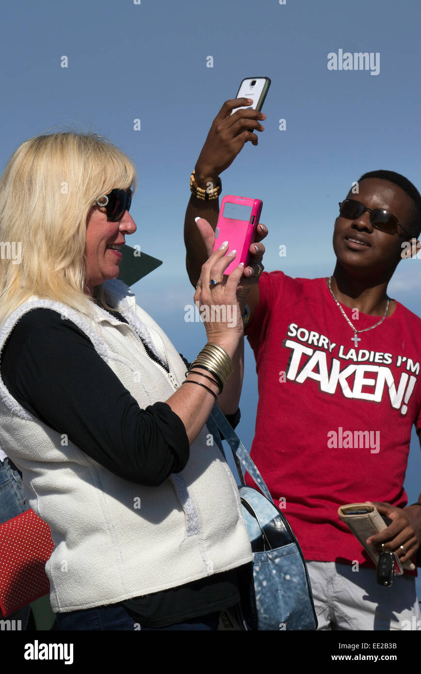 Two people, (one black, one white), on Table Mountain, Cape Town, taking selfies with their mobile phones. Stock Photo