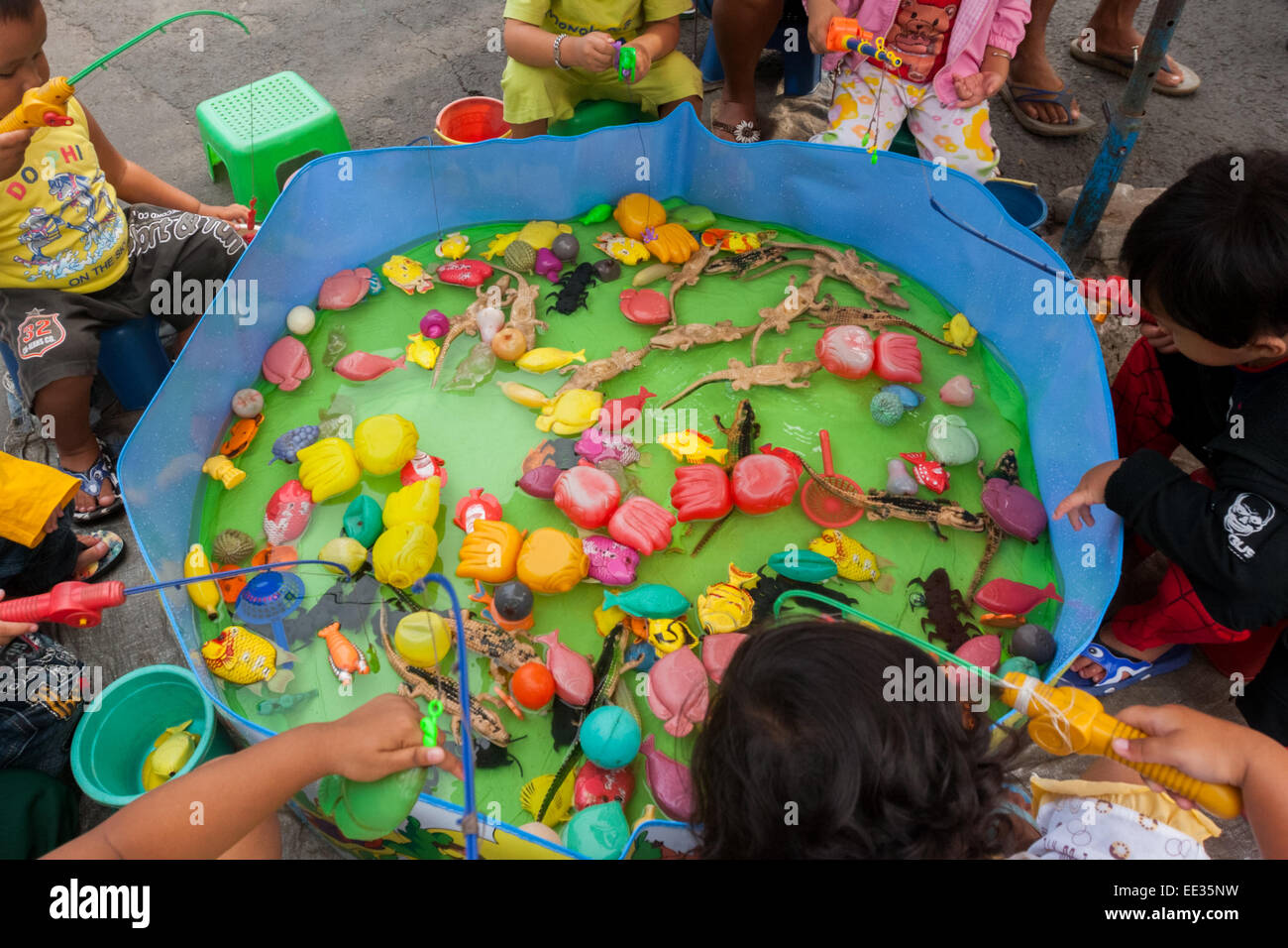 Children play fishing game on a small pond containing plastic toys at a street market near