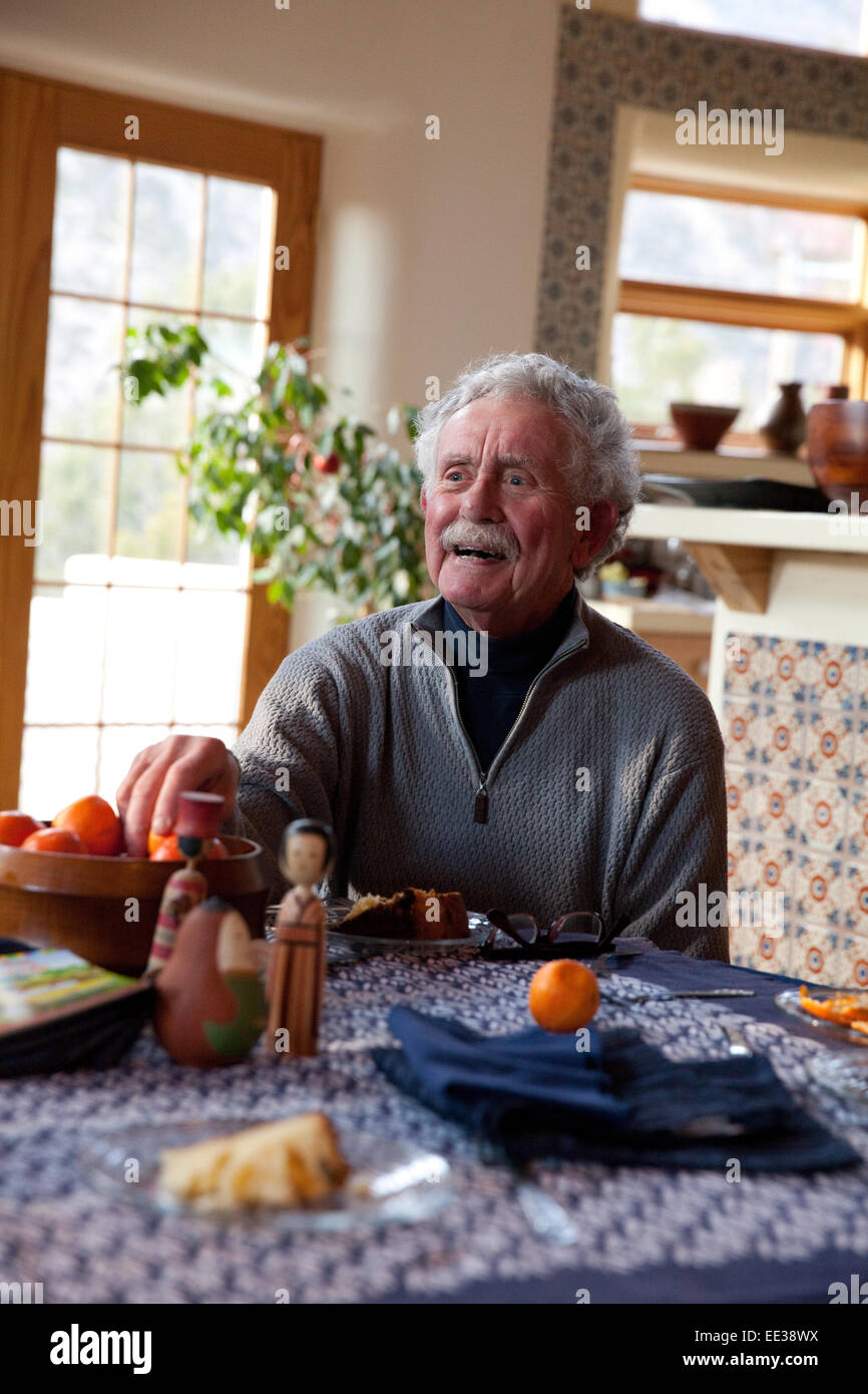 Elderly man laughing at dining table Stock Photo