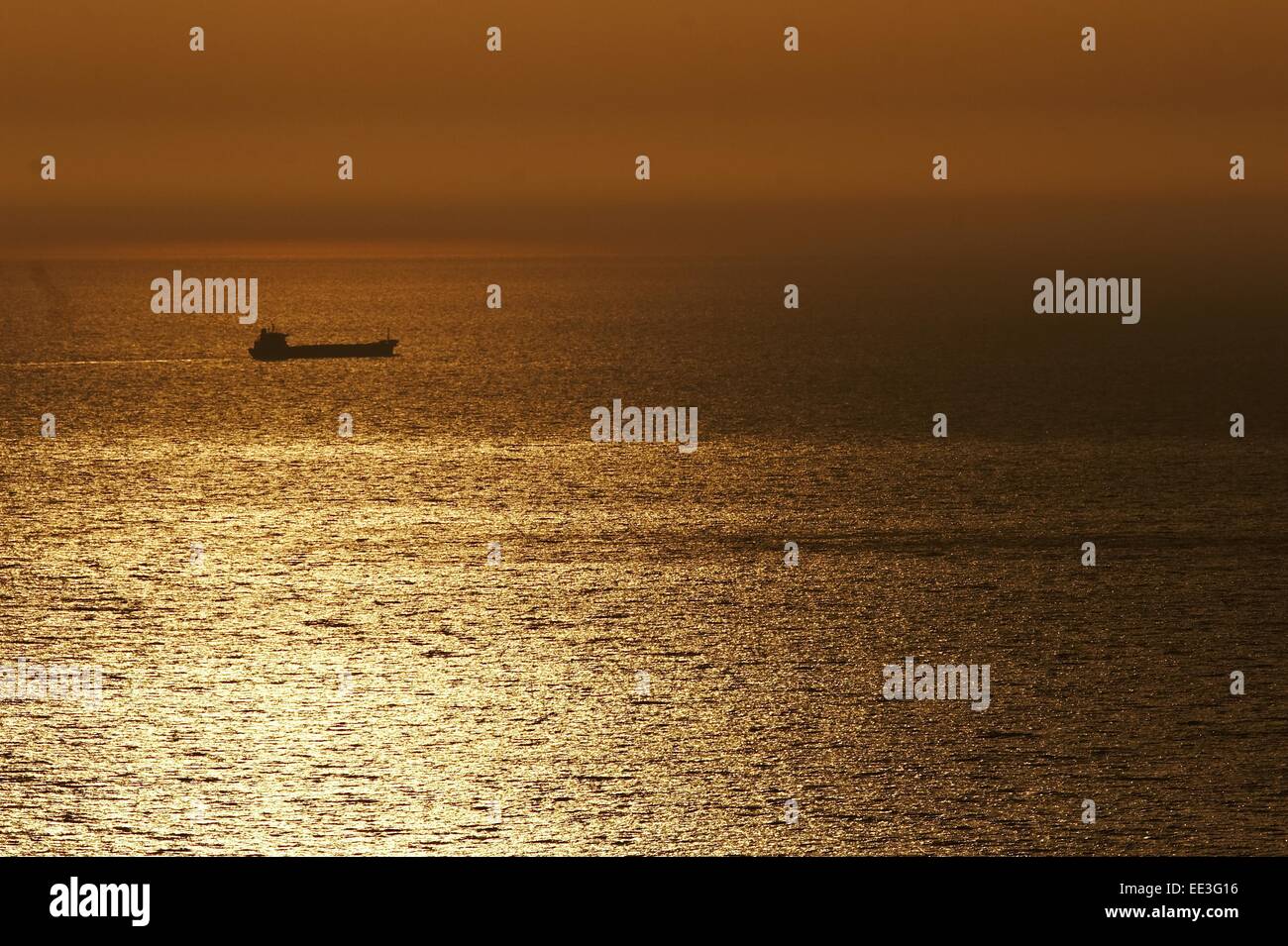 Cargo ship during sunset on open ocean with reflections Stock Photo