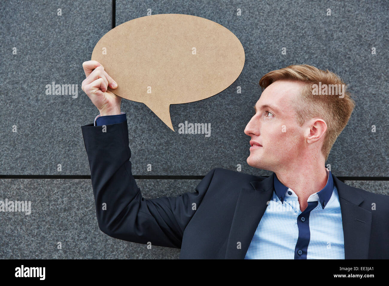 Young business man holding empty speech bubble in front of a wall Stock Photo