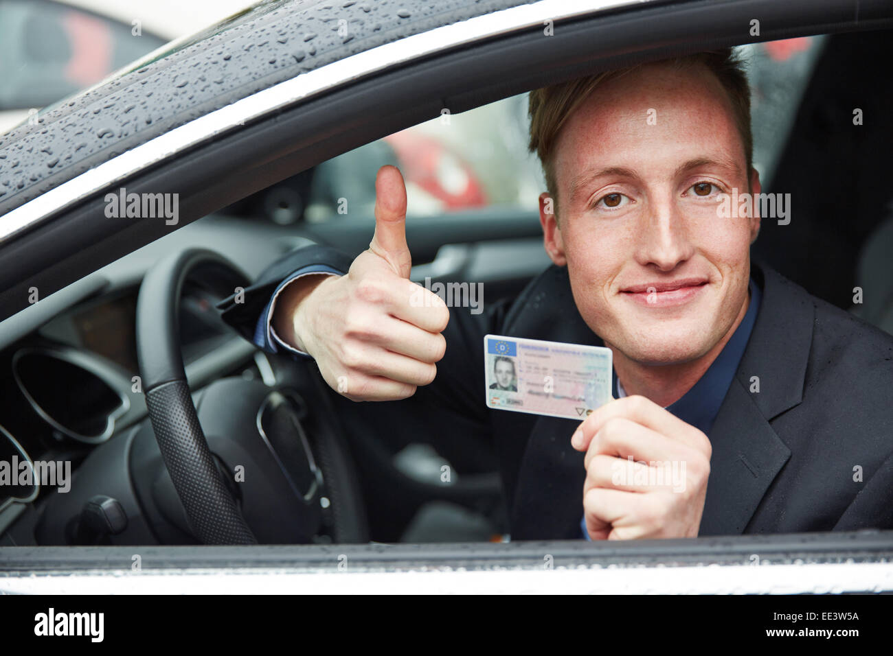 Young proud man in a car holding drivers licence and his thumps up Stock Photo