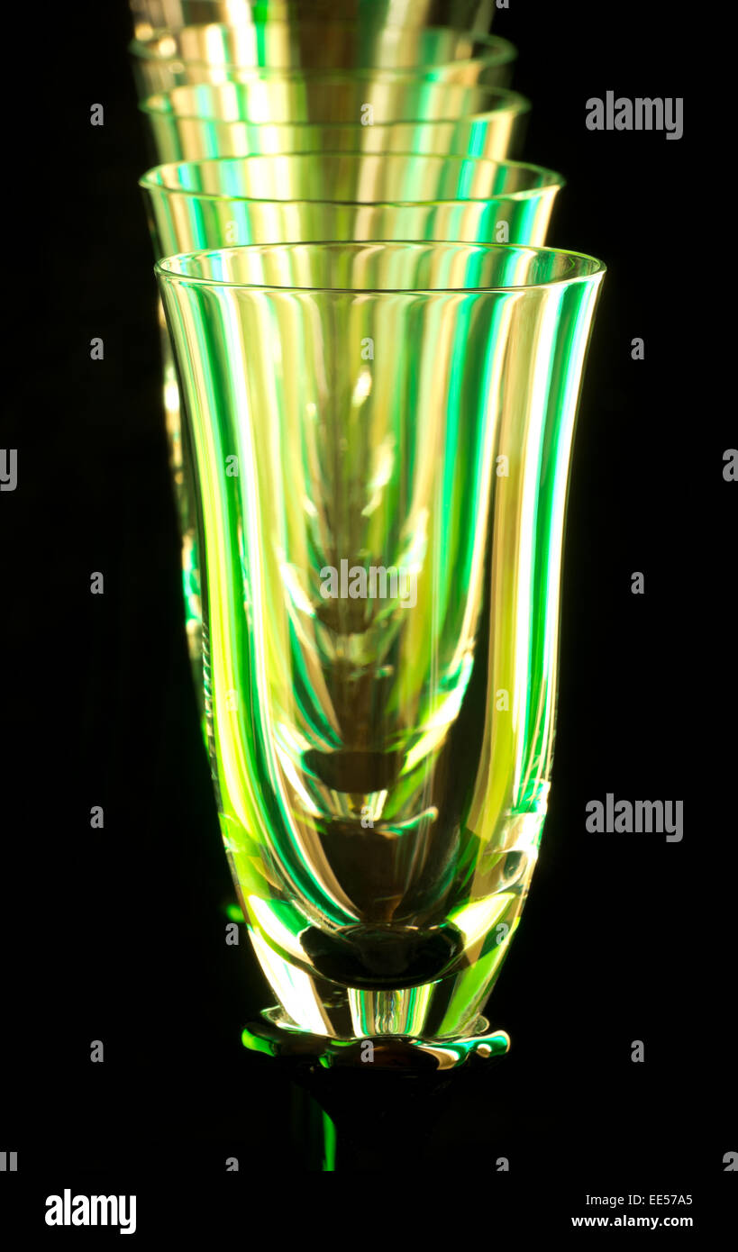 abstract of flute glasses or champagne stemware lined up in a row closeup isolated against black Stock Photo