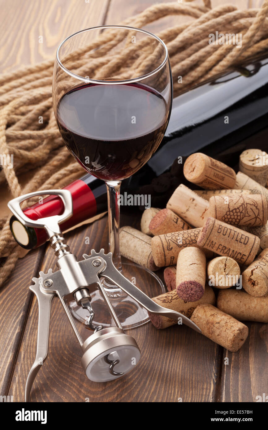 Glass of red wine, bottle, heap of corks and corkscrew on rustic wooden table Stock Photo