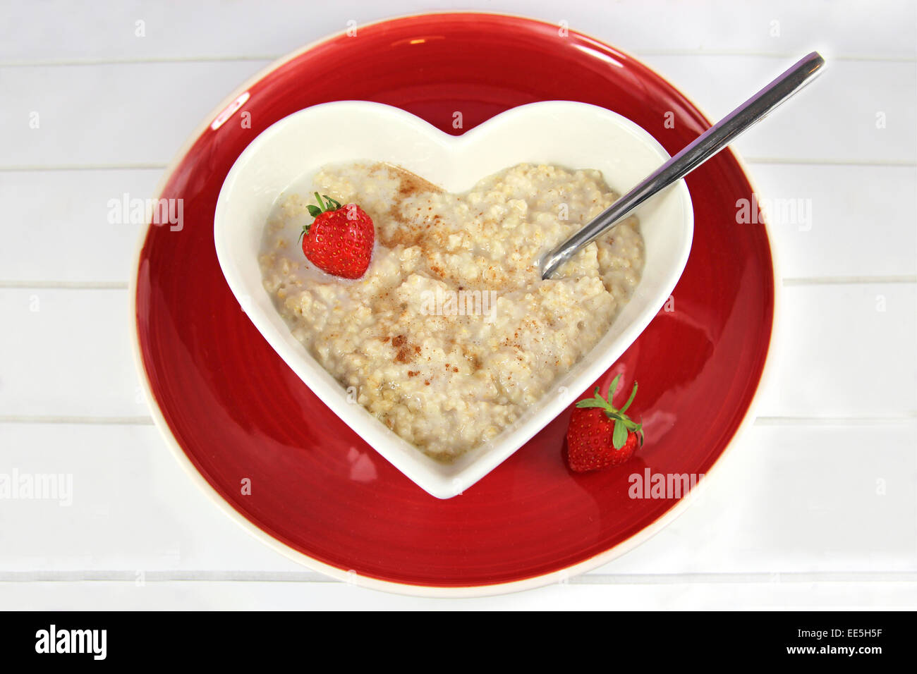 Porridge/oatmeal with honey cinnamon in a heart shaped bowl on a red plate  with a strawberry garnish. On white wood background Stock Photo - Alamy