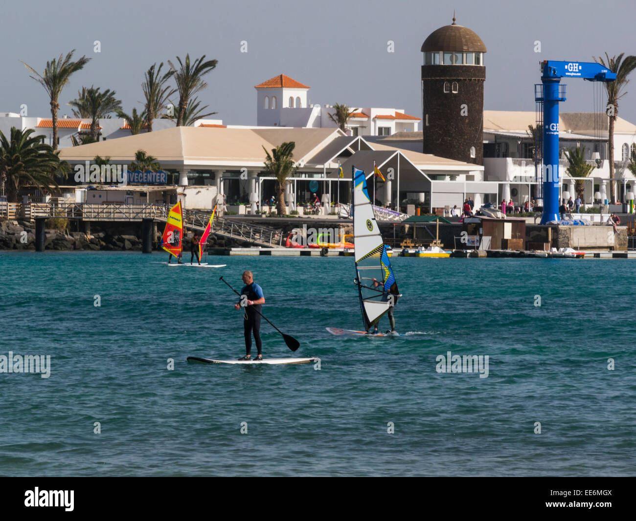 Man standing up paddling surfboard wind surfers in Caleta de Fuste bay