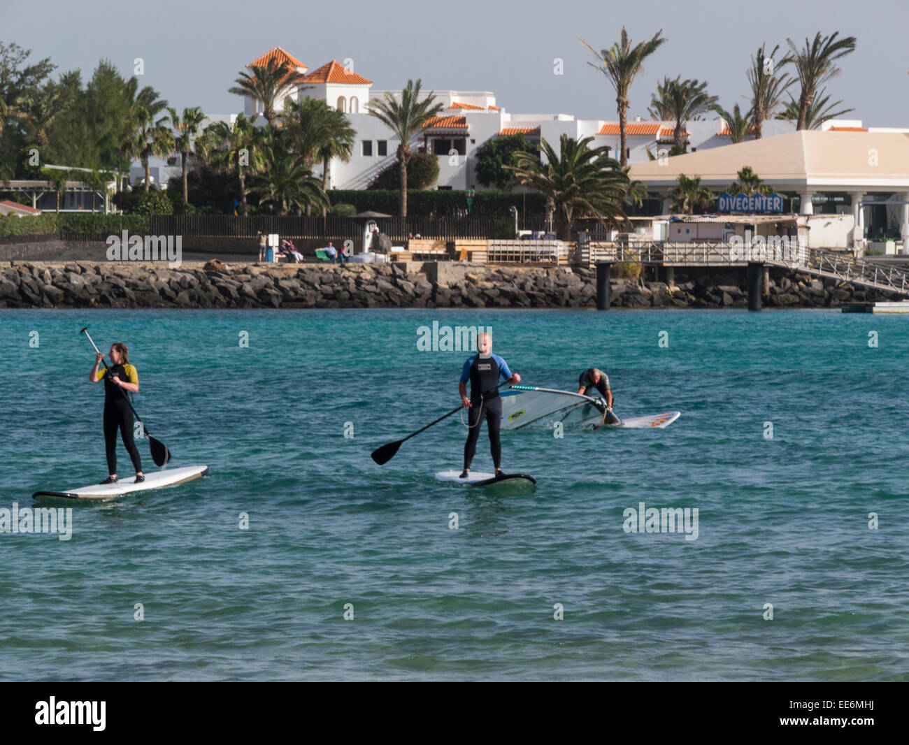 Man and woman standing up paddling surfboard and windsurfer in Caleta