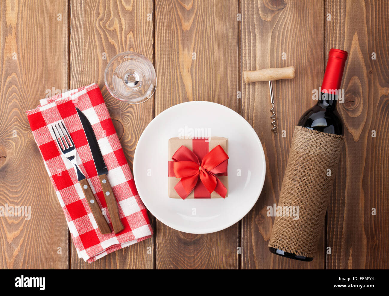 Table setting with gift box on plate, wine glass and red wine bottle ...