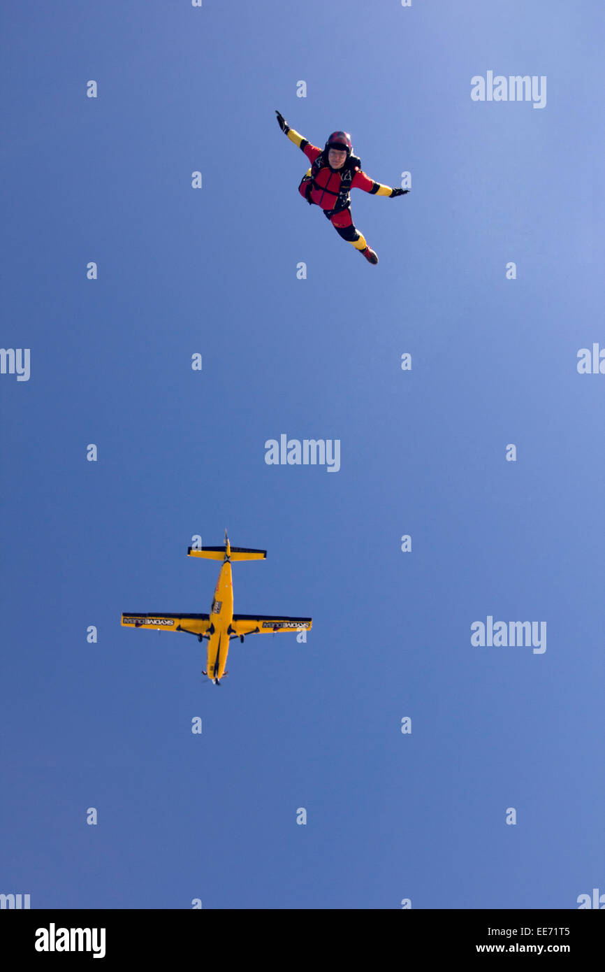 This skydiving girl jumped out of the yellow aircraft at 13'000ft altitude. Thereby she has fun and is smiling in the blue sky. Stock Photo
