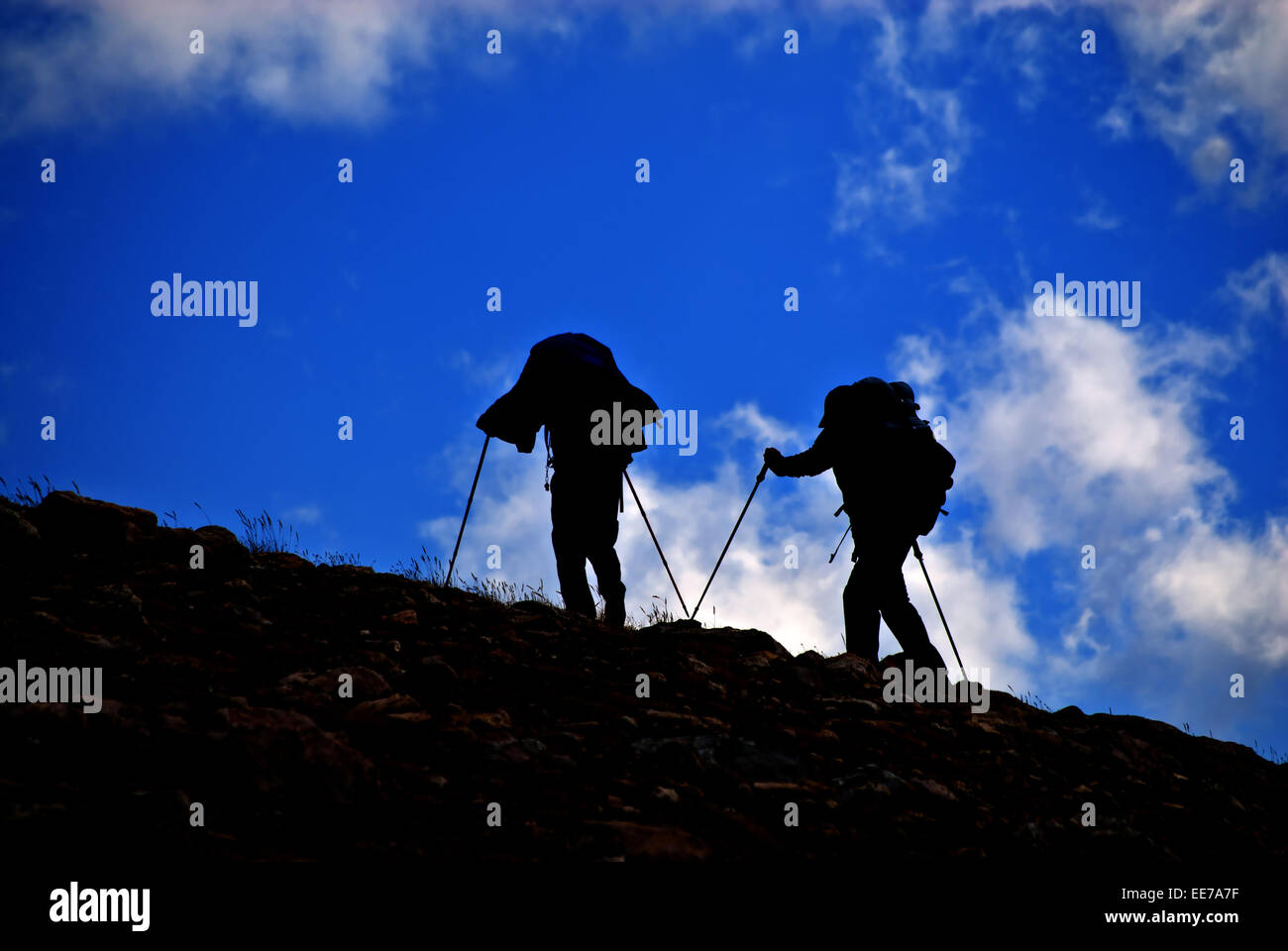Silhouette of people hiking on mountainside with clouds in sky Stock Photo