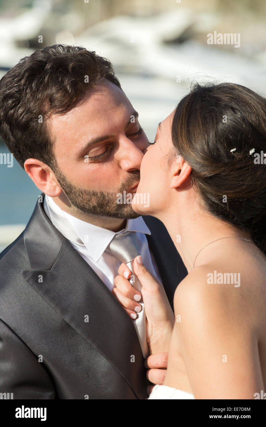 Married couple in day of their wedding. Bride pulls the tie of the groom while kissing him. Stock Photo
