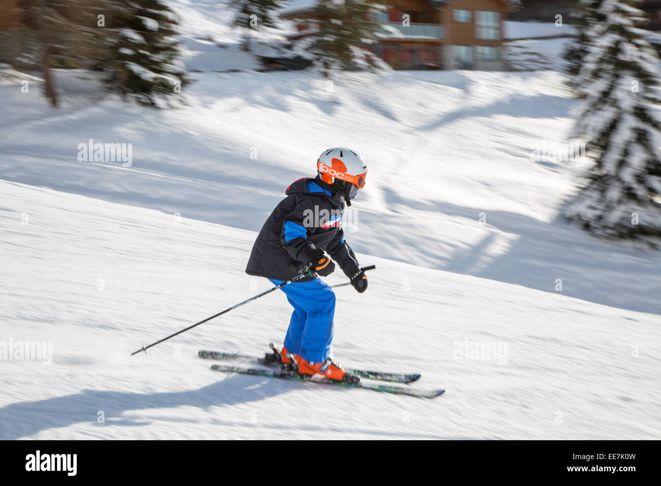 Child wearing ski helmet skiing down ski slope in winter sports resort in the Alps Stock Photo