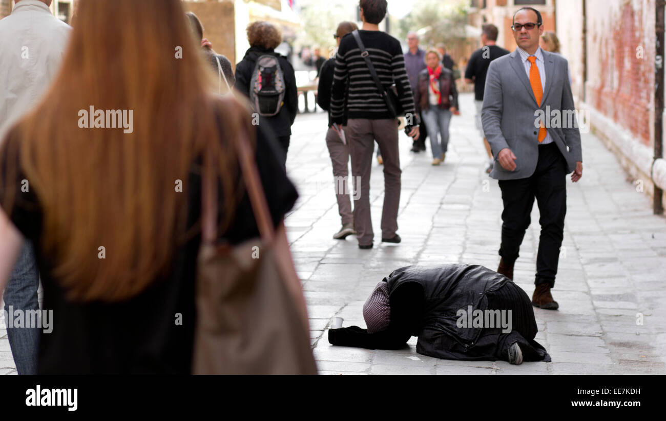 People walking past homeless person begging on floor. Venice, Italy Stock Photo