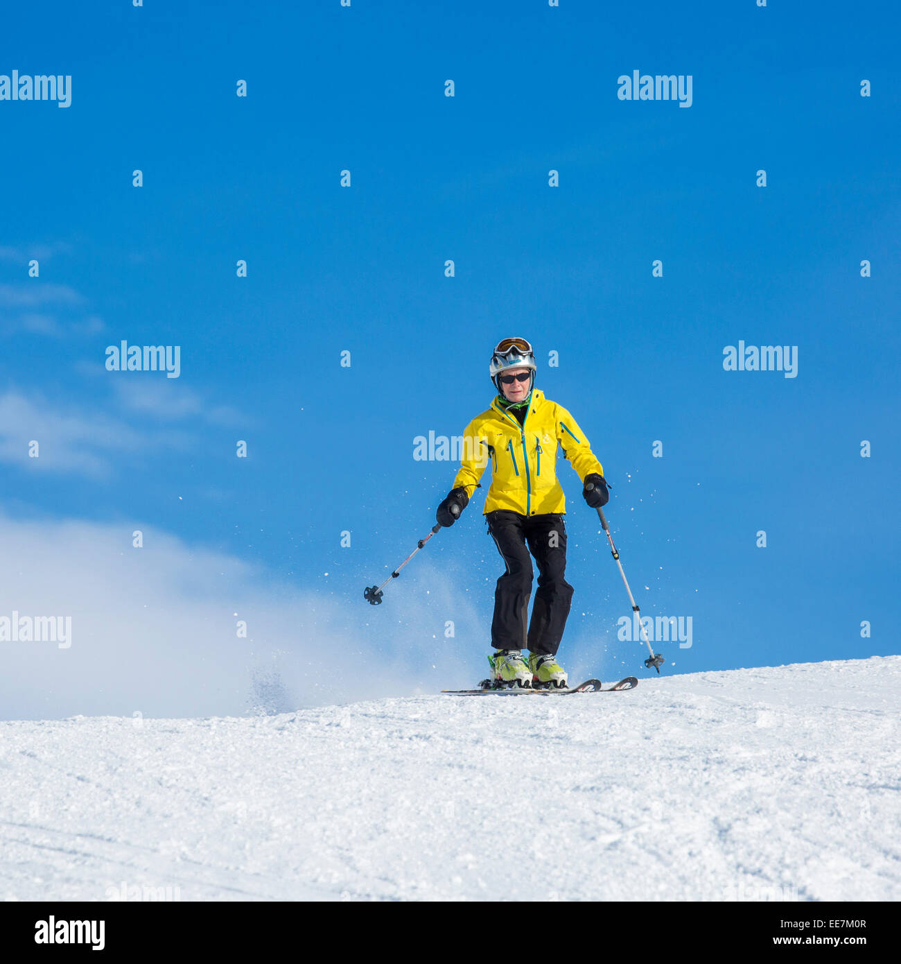 Elderly female skier wearing ski helmet skiing down ski slope in winter sports resort in the Alps Stock Photo