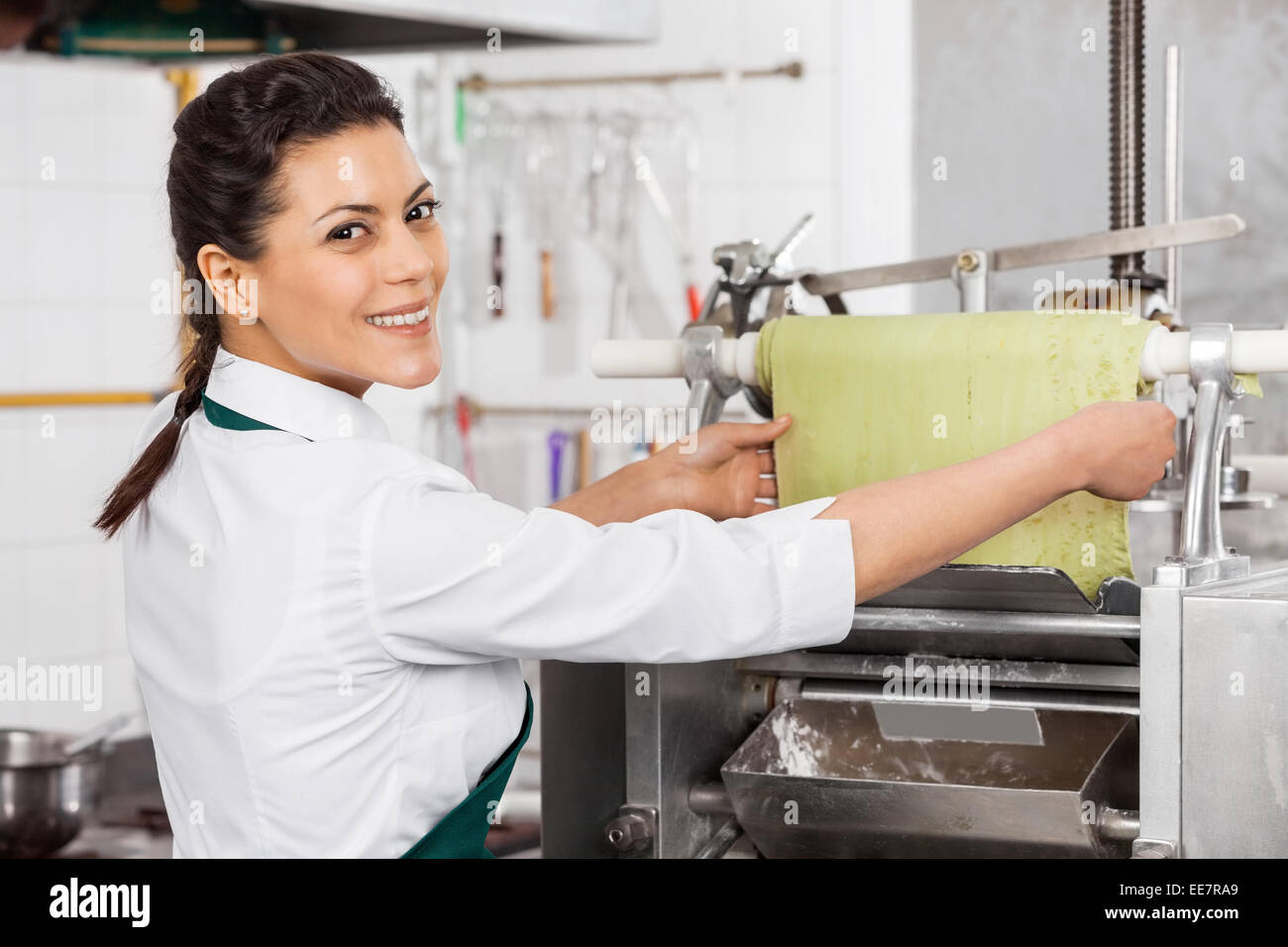 Female Chef Processing Green Pasta Sheet In Machine Stock Photo