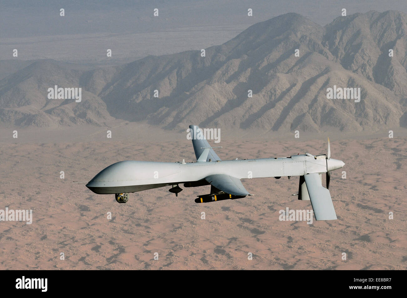 Armed MQ-1 Predator unmanned aircraft carrying 2 Hellfire missiles flying over desert landscape Stock Photo