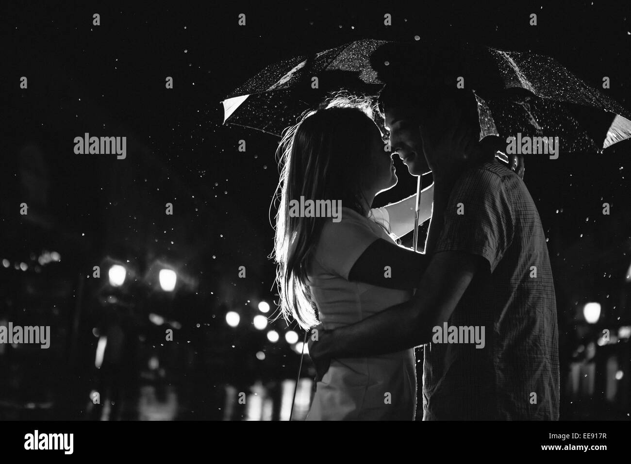 Love in the rain / Silhouette of kissing couple under umbrella Stock Photo