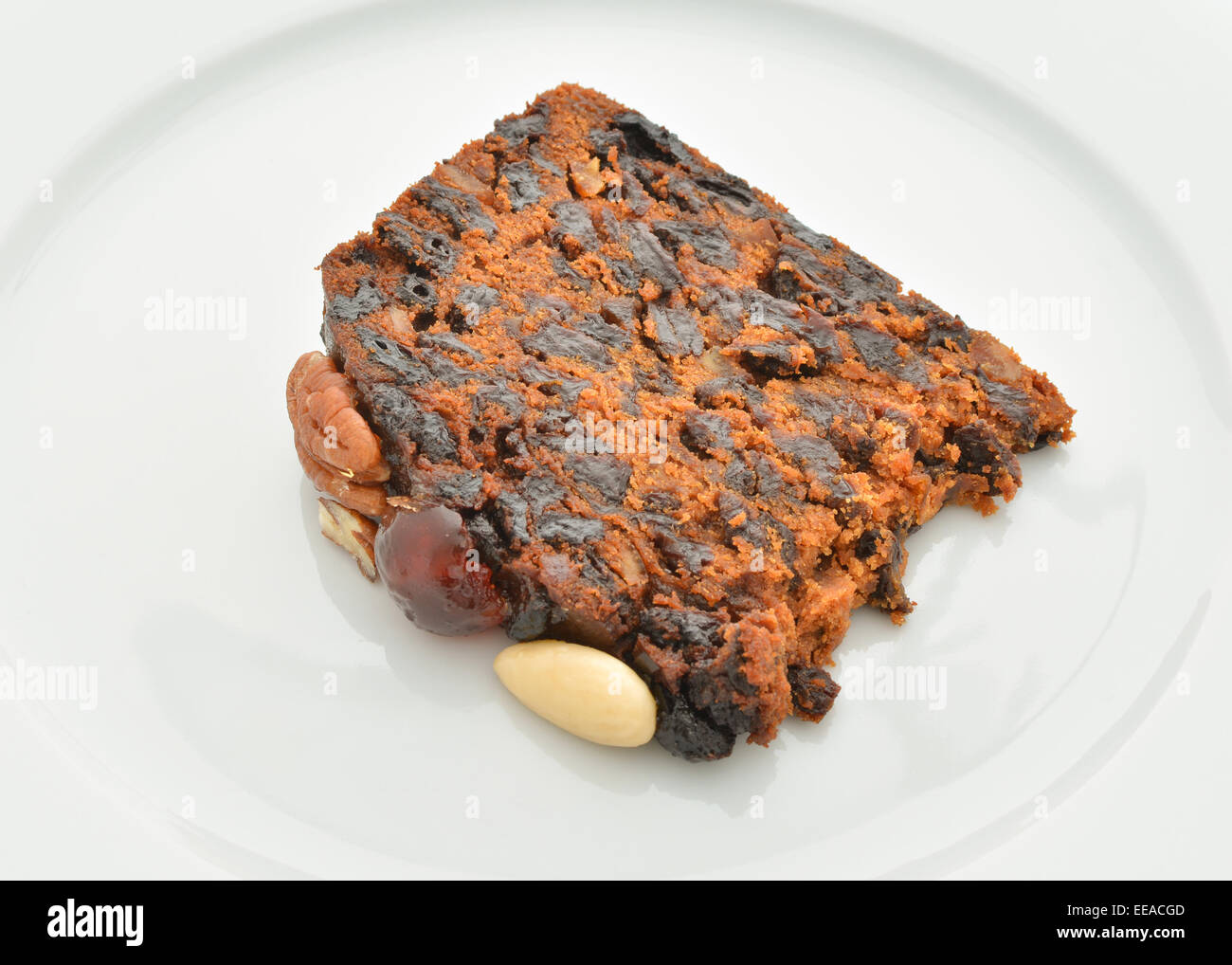 Slice of homemade fruitcake decorated with nuts and cherries on white plate Stock Photo
