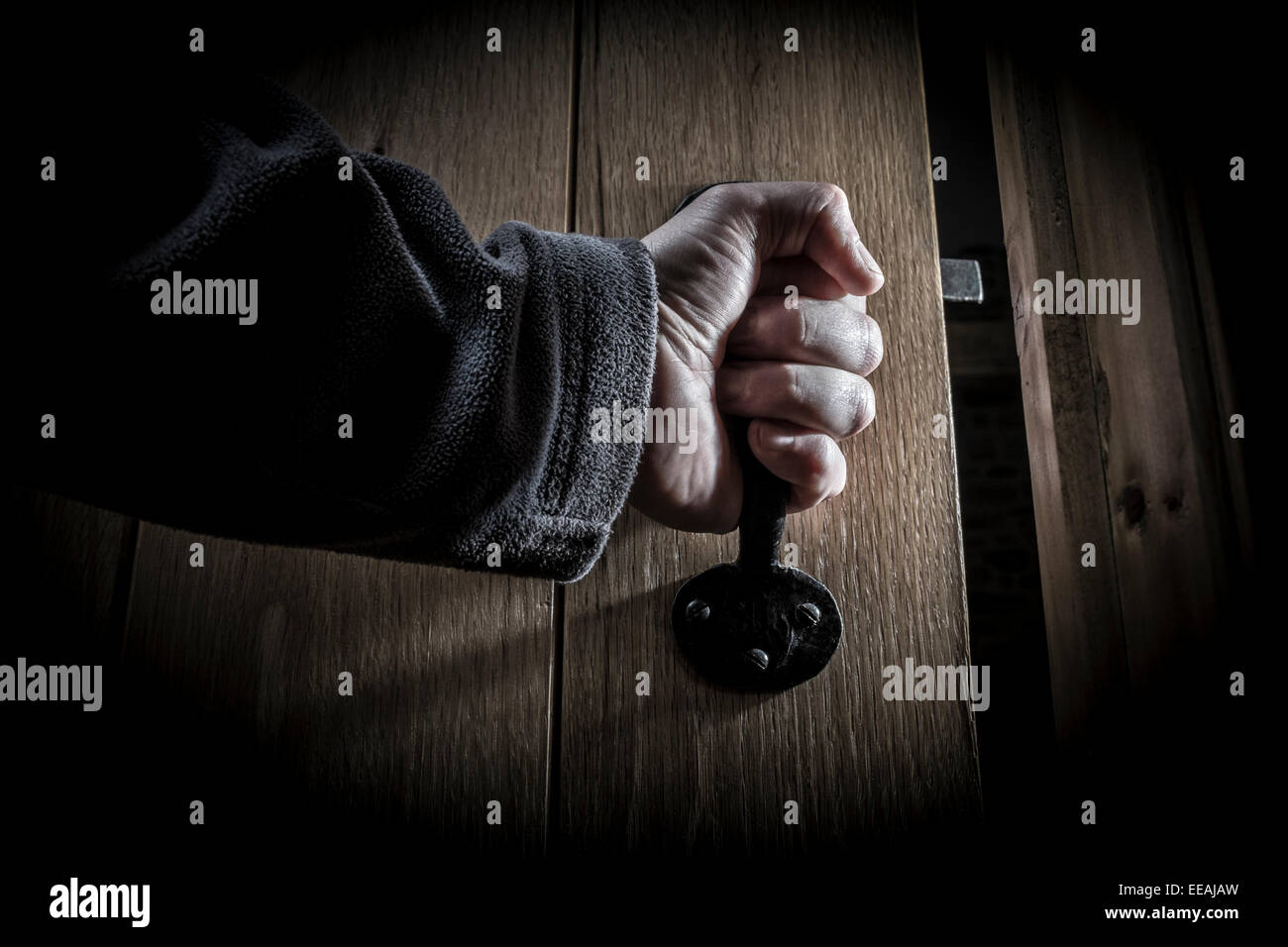 A man's hand opening a door into a dark room. Stock Photo