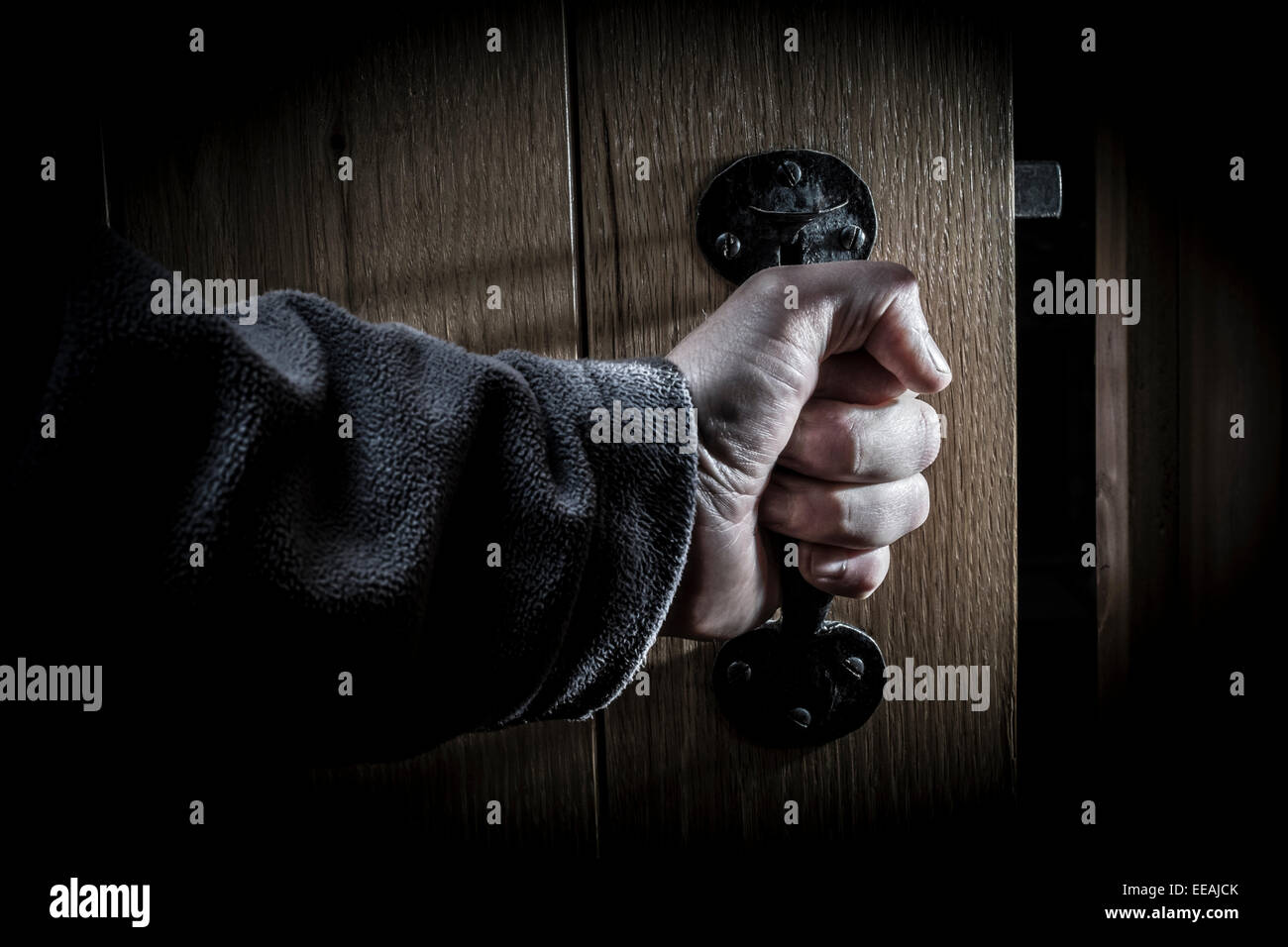 A man's hand opening a door into a dark room. Stock Photo