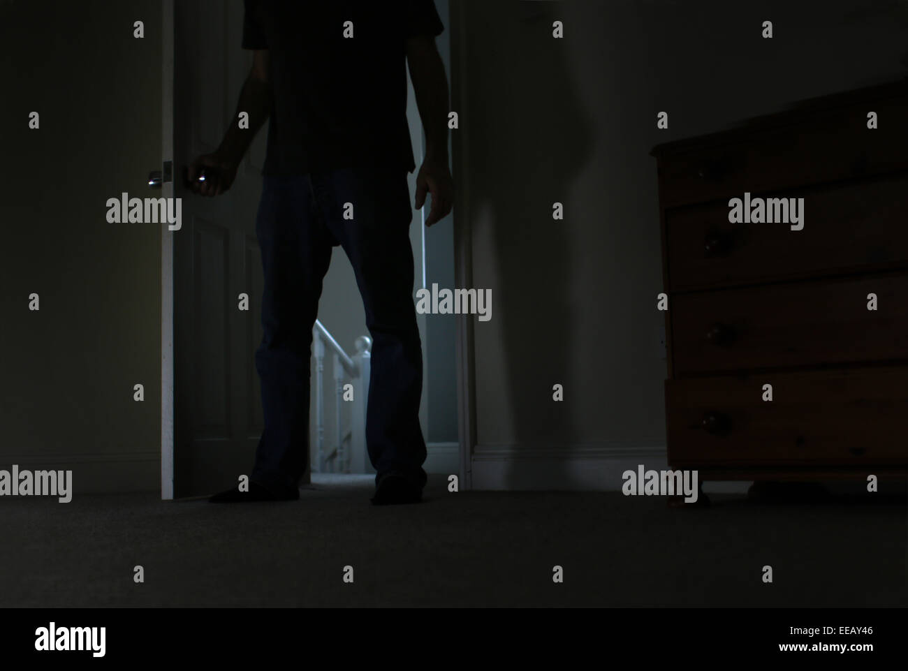 Silhouette of a man, lower body shot, entering a dark room. Stock Photo