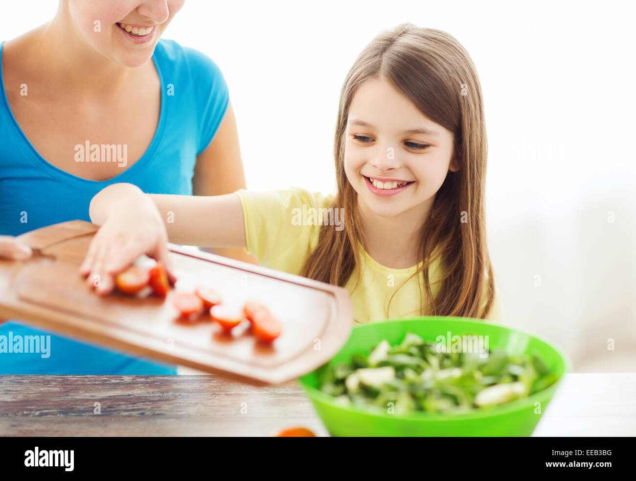 little girl with mother adding tomatoes to salad Stock Photo