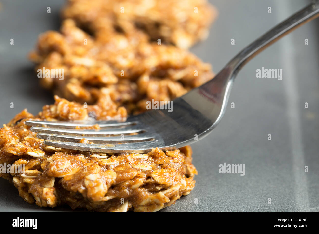 Fork pressing down raw oatmeal cookie dough on baking sheet Stock Photo