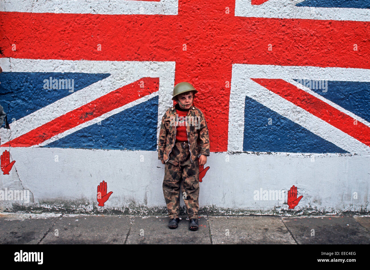 BELFAST, NORTHERN IRELAND - SEPTEMBER 1971. Child playing as soldier in front of Union Jack flag mural in Protestant part of Belfast during The Troubles,  Northern Ireland. Stock Photo