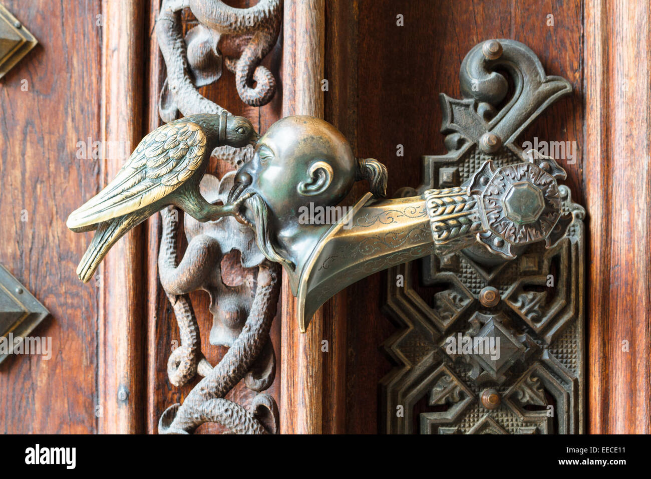 An ornate doorhandle of a castle where an asian man's head is pecked by a bird Stock Photo
