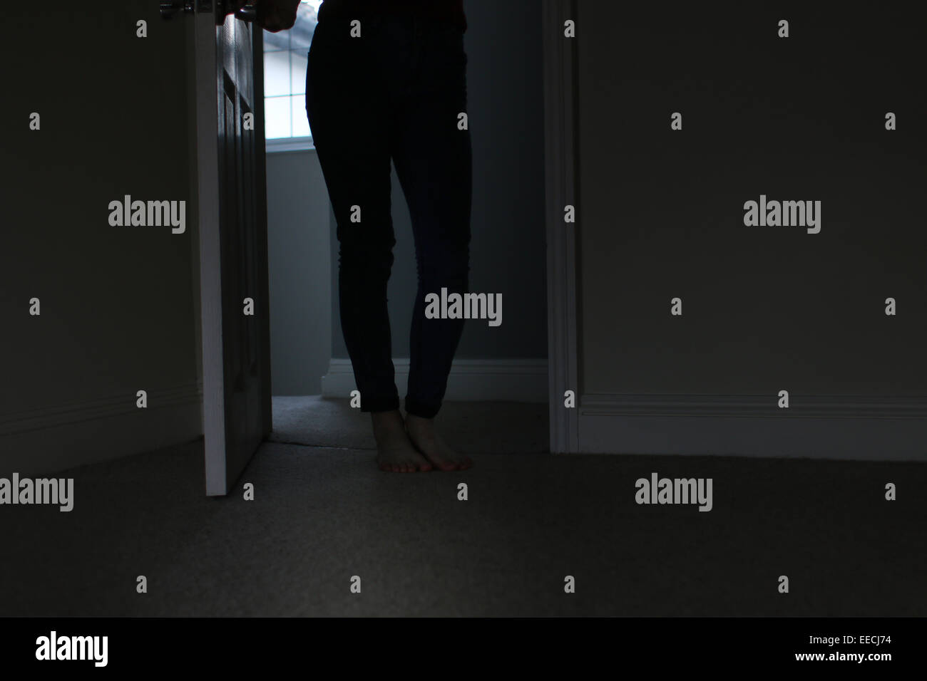 Silhouette of a female, lower body shot, entering a dark room. Stock Photo