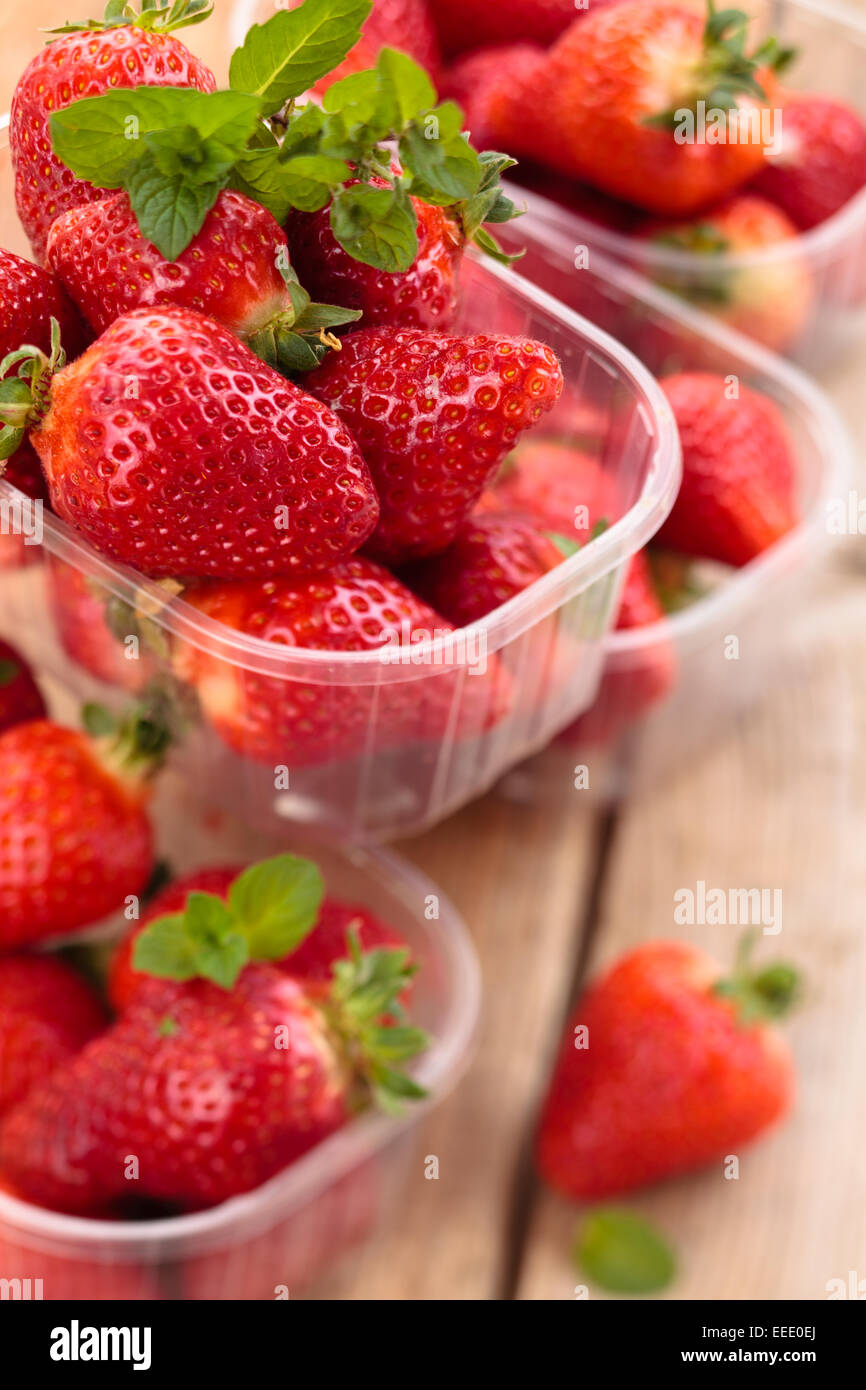 Fresh strawberries in containers and mint leaves on wooden table Stock ...
