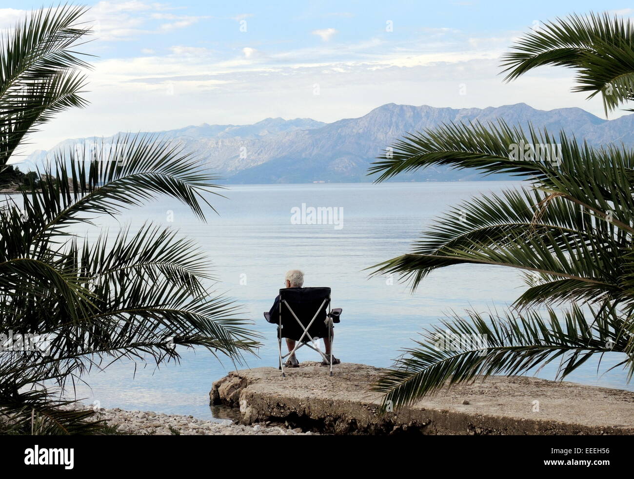 A pensioner sitting in a folding chair on the coast of the dalmatian island of Korcula (Croatia) enjoys the view to peninsula Peljesac, sun and sea, on September, 24, 2014. Stock Photo