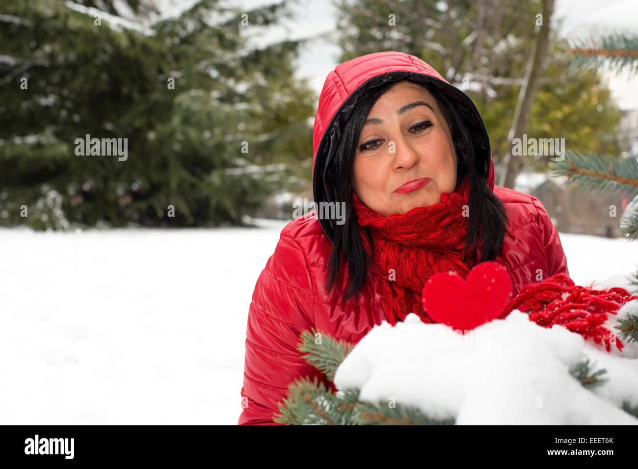 Black haired Turkish upset women looking at red heart on snow and celebrating Valentine's day alone Stock Photo