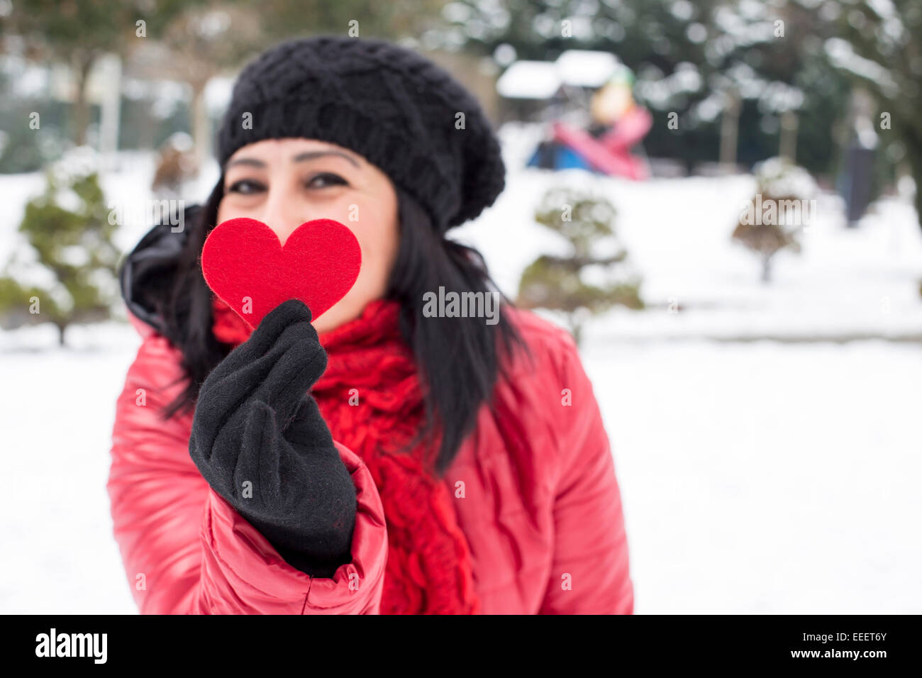 Black haired Turkish women holding a red heart with black warm wool gloves and celebrating Valentine's day with snowy background Stock Photo