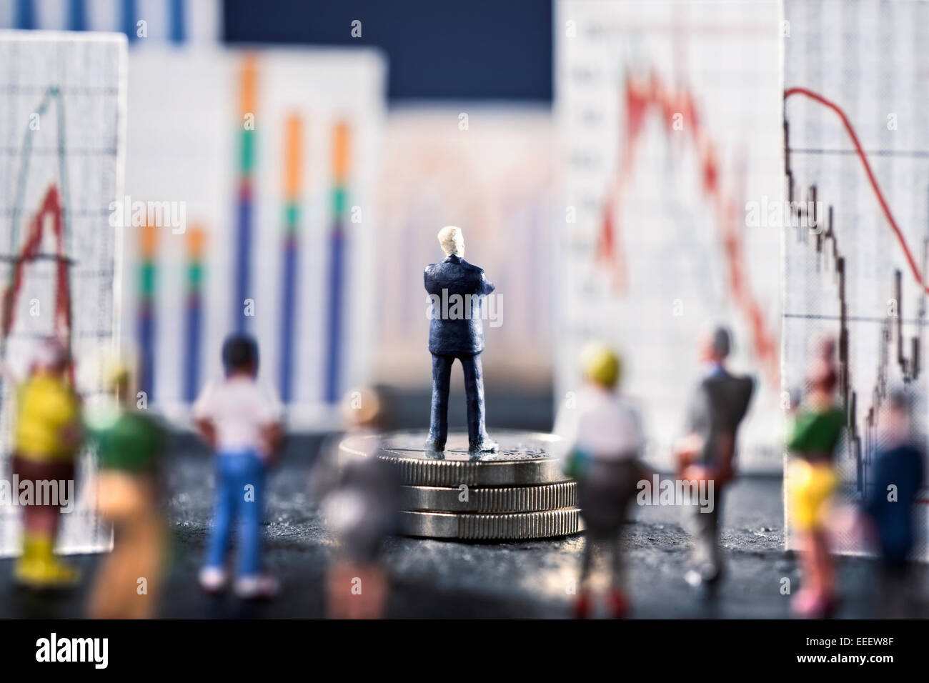 Banker looks on boards with various charts, symbolizing the ups and downs in the markets. He stands on a base of coins. Stock Photo