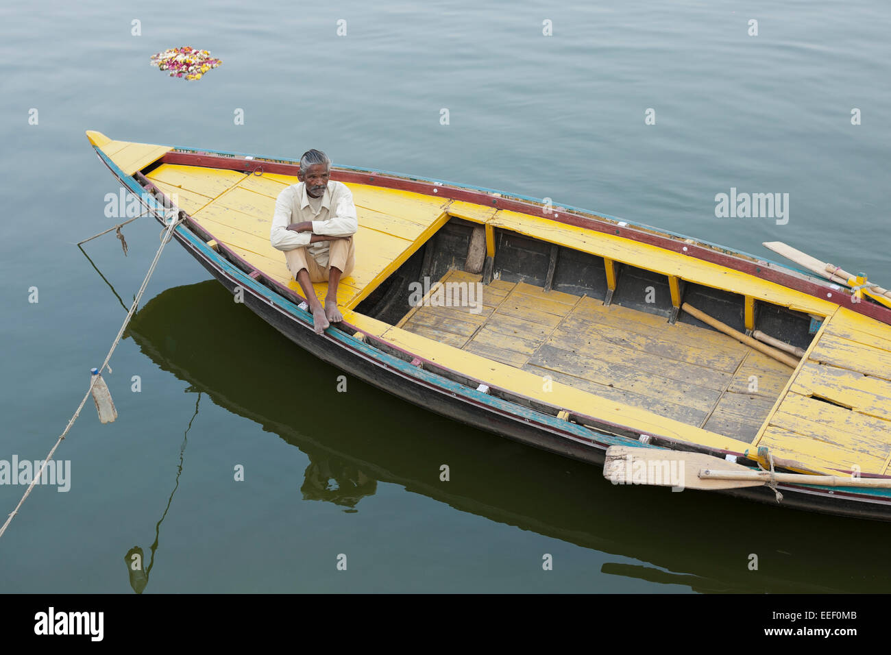 Varanasi, India. Row boat on the Ganges river. Boatman waiting for customers, votive flowers floating by Stock Photo