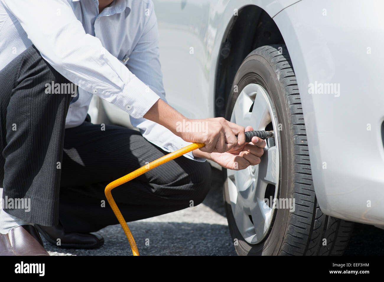 Asian driver checking air pressure and filling air in the tires of his