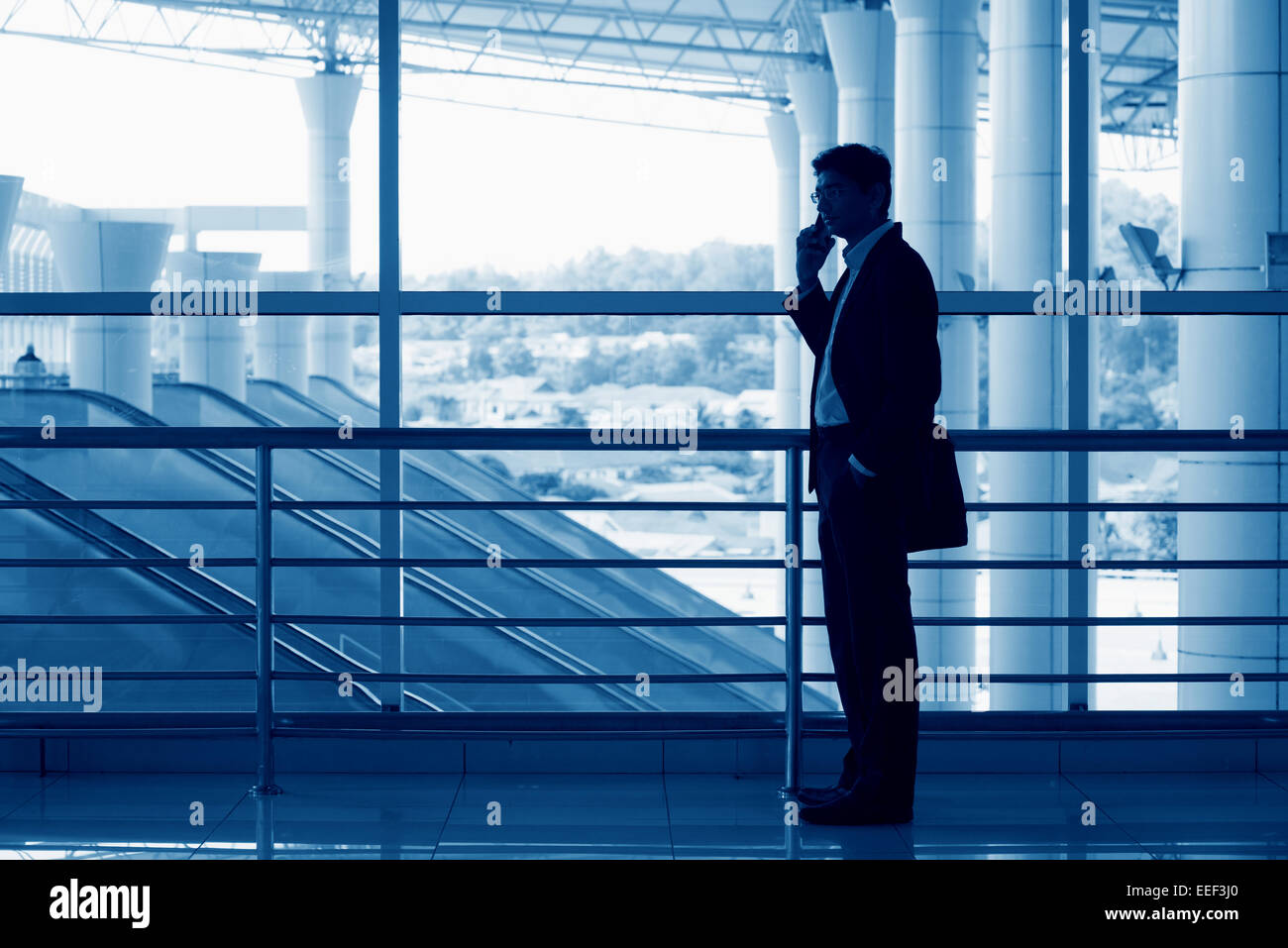 Silhouette of Asian Indian man on mobile phone in modern office building, blue tone. Stock Photo