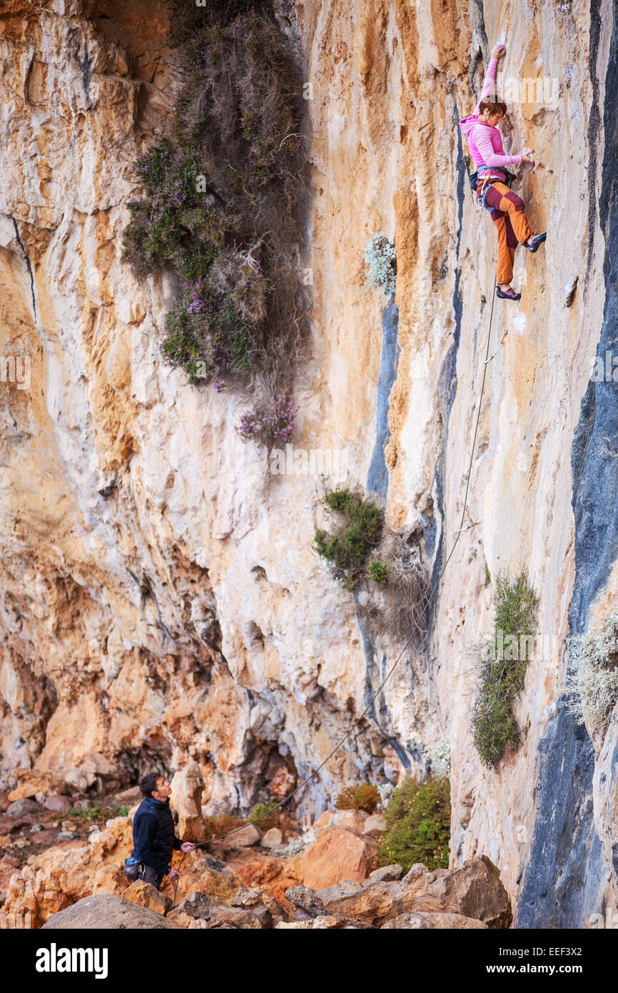 Young woman lead climbing on natural cliff, belayer watching her Stock